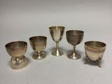 six silver goblets and cups on a white surface