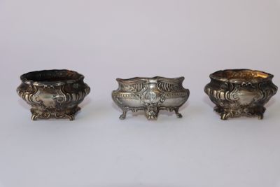 trois vases en argent posés l'un à côté de l'autre sur une surface blanche