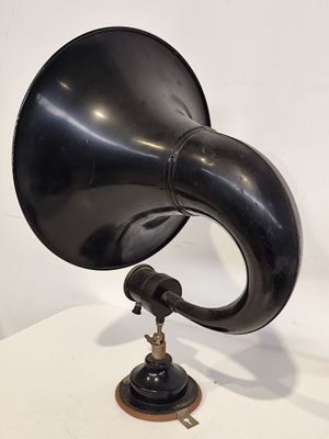 un gramophone noir posé sur un socle en bois, lui-même posé sur une table blanche