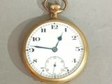 a gold pocket watch with a white face on a white surface