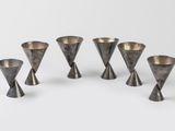 six vases en argent sont disposés en cercle sur une surface blanche