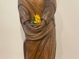statue en bois représentant une femme tenant une fleur jaune dans ses mains