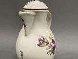 a white vase with purple flowers on it on a gray surface