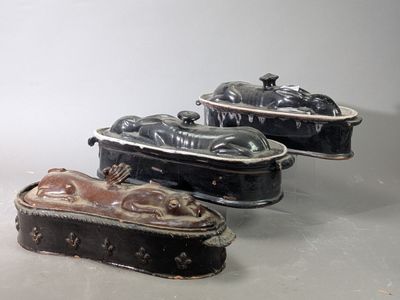 trois plats à couvercle, noirs et marron, posés sur une table