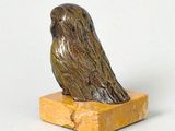 statue of a bird sitting on a wooden block on a white surface