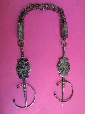 two silver necklaces on a pink background with a chain around them