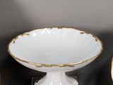 a white bowl with gold trim on a clear pedestal