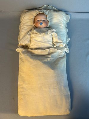 une poupée allongée dans un lit, recouverte d'une couverture