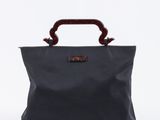 un sac noir muni d'une poignée en bois posé sur une surface blanche