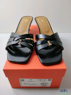Les chaussures noires sont posées sur la boîte orange qui se trouve sur la table.