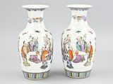 pair of chinese vases with figures on them sitting on a table