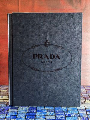 un livre Prada noir posé sur un sol carrelé