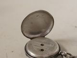 a silver pocket watch sitting on a table with a keychain