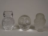 trois figurines de chouettes en verre posées les unes à côté des autres sur une surface blanche