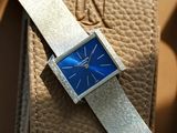 a silver and blue watch sitting on a tan leather bag