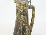 a brown and black pitcher with a green bead on it