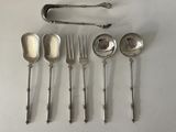 six spoons and a fork are arranged on a white surface