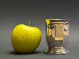 a silver vase next to a green apple on a table