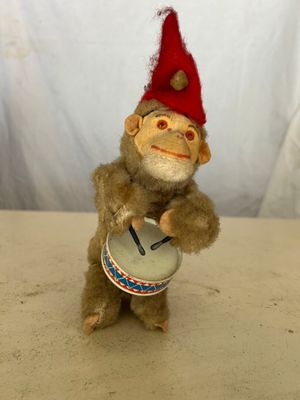 un petit singe en peluche coiffé d'un bonnet rouge et tenant un tambour