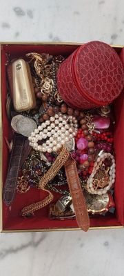 une boîte rouge remplie de bijoux variés, posée sur un plan de travail en marbre