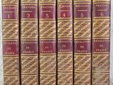 six old books are lined up in a row on a table