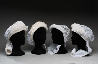 trois têtes de mannequins noires coiffées de bonnets blancs, posées sur une table