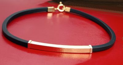 a black leather bracelet with a gold bar on a red surface