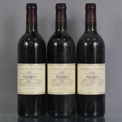 trois bouteilles de vin rouge sont posées sur une table en verre devant un mur gris