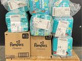 Des cartons de couches sont empilés sur une palette devant un mur noir