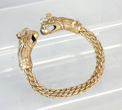 gold plated bracelet with a dragon head on it on a clear surface