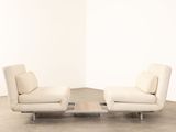 pair of white leather lounge chairs and a coffee table in an empty room