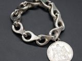 a close up of a silver bracelet with a coin on it