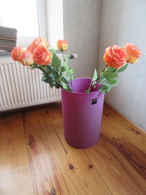 un vase violet contenant des roses orange, posé sur un parquet