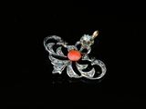 an image of a silver and coral colored broochle on a black surface