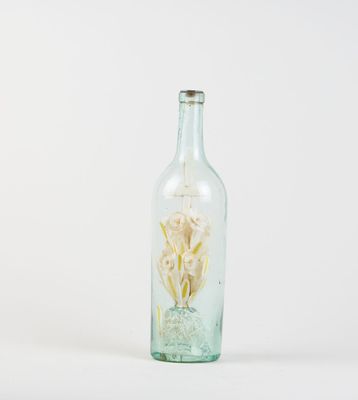 a glass bottle with a flower inside of it on a white surface