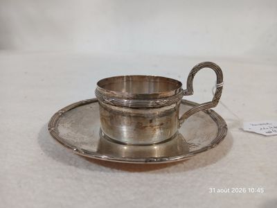 une tasse et une soucoupe en argent posées sur une soucoupe, sur une table
