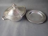 a silver pot with a lid and a silver plate on a table