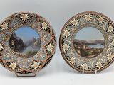 two decorative plates with a painting of a mountain scene on them