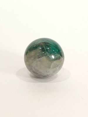 une boule de marbre verte et blanche posée sur une surface blanche, avec un fond blanc