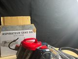a red vacuum on a wooden table next to a box and a light