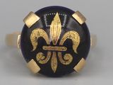 une image représentant une bague dorée et noire ornée d'une fleur de lys