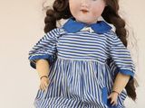 une poupée à l'ancienne, assise sur une surface blanche, vêtue d'une robe à rayures bleues et blanches