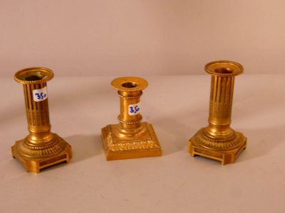 trois bougeoirs dorés posés sur une surface blanche