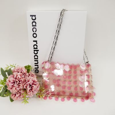 a pink purse with a chain hanging from it next to a pink flower