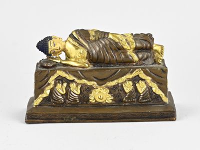 statue en bronze représentant une personne allongée sur un lit orné d'une décoration dorée