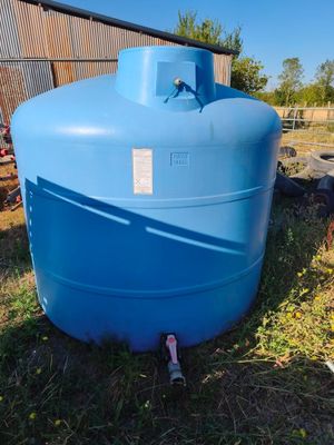 un grand réservoir d'eau bleu posé dans l'herbe, près d'une clôture