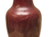 un vase rouge reposant sur un socle en bois, sur fond blanc