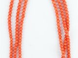un collier de perles orange muni d'un fermoir en argent, sur fond blanc