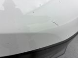 the rear end of a white car with a person standing in the background