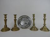 three brass candlesticks and a silver plate on a white surface